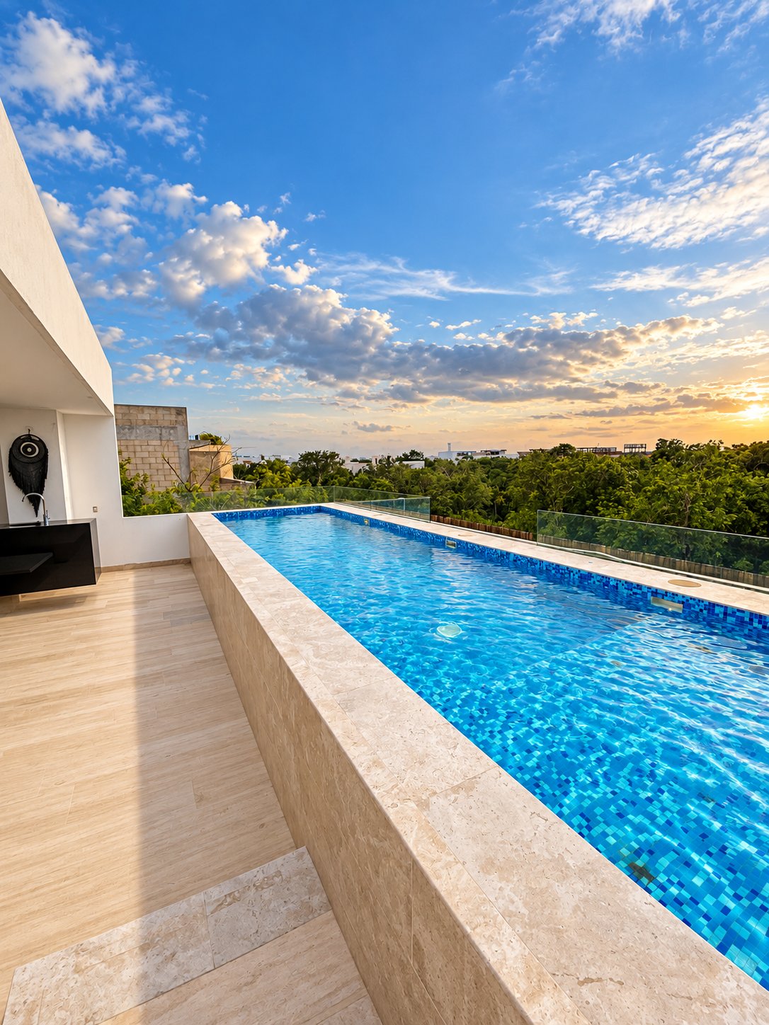 Rooftop pool with glass railings overlooking treetops at sunset.