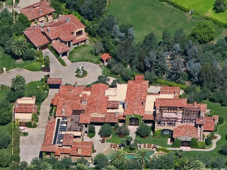 Aerial view of a sprawling estate with red-tile roofs, landscaped grounds, and a circular driveway.