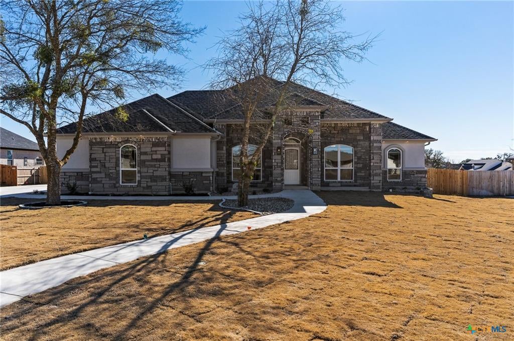 Single-story stone-front home with an arched entry and curved walkway across a dormant lawn.