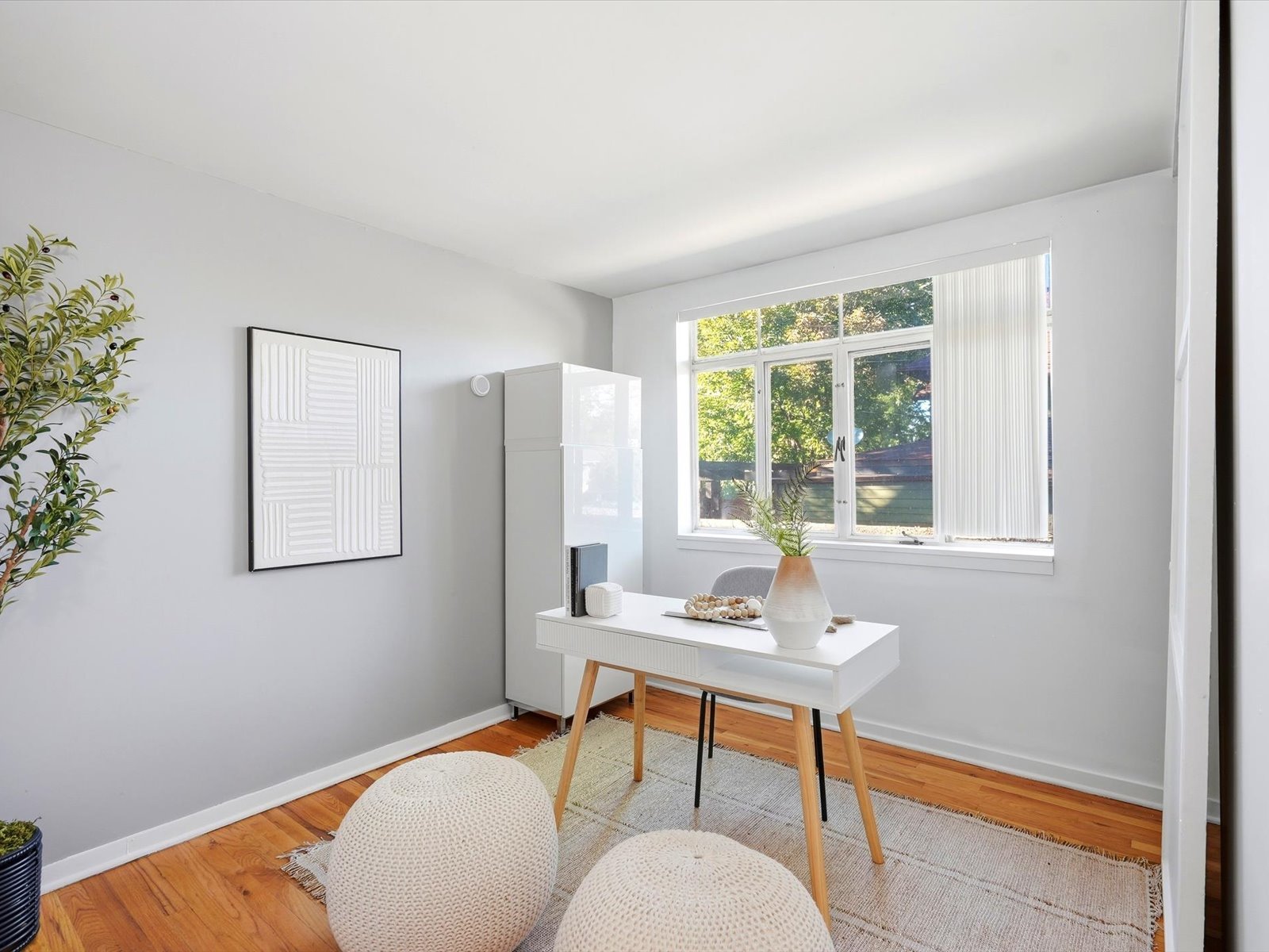 Bright home office with a white desk, abstract wall art, and a large window overlooking trees.