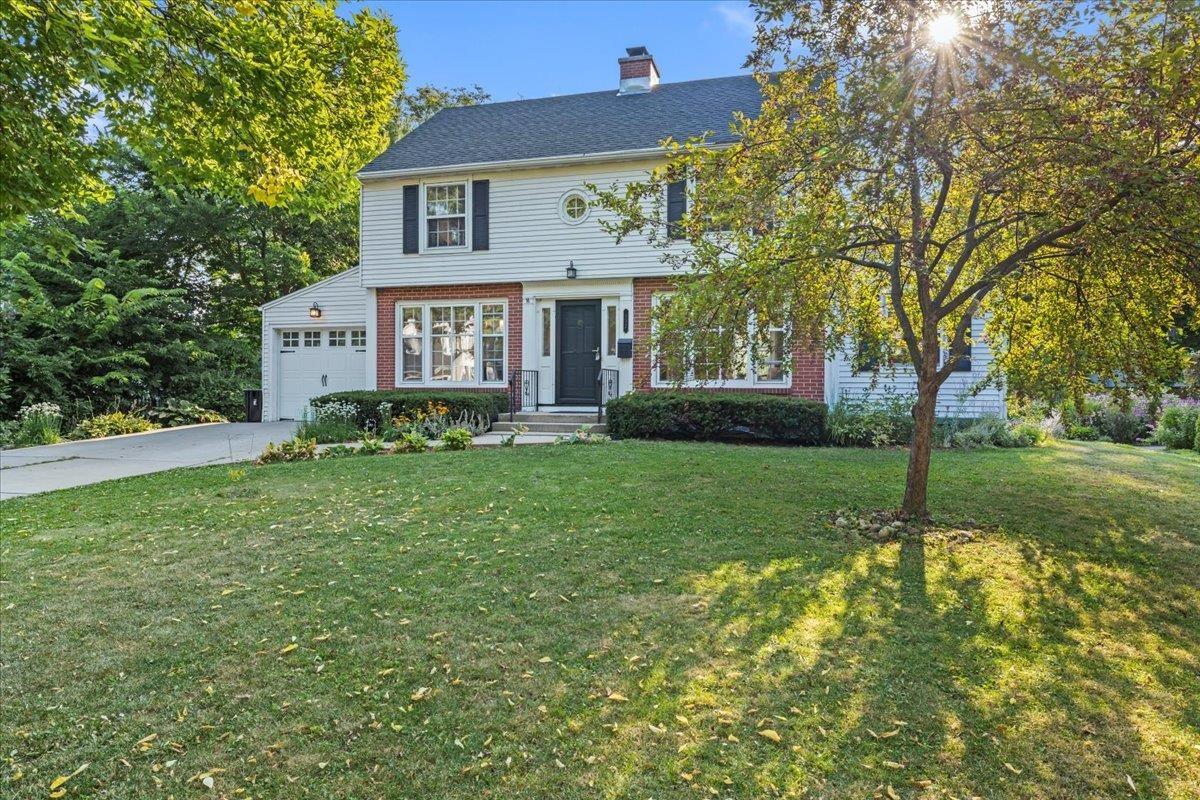 A 1940s colonial home with white siding, brick accents, and black shutters on a sunny lawn in an older Madison neighborhood.