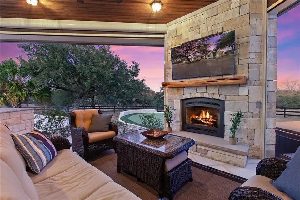Covered patio with wicker seating, a stone fireplace, and a pool at dusk.