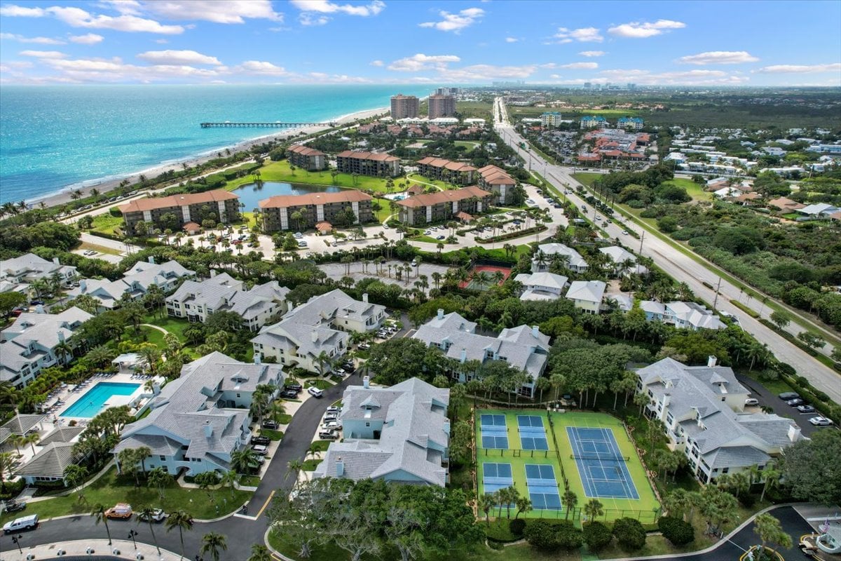 Aerial view of coastal condominiums, with a lagoon, tennis courts, pools, beach, and ocean.