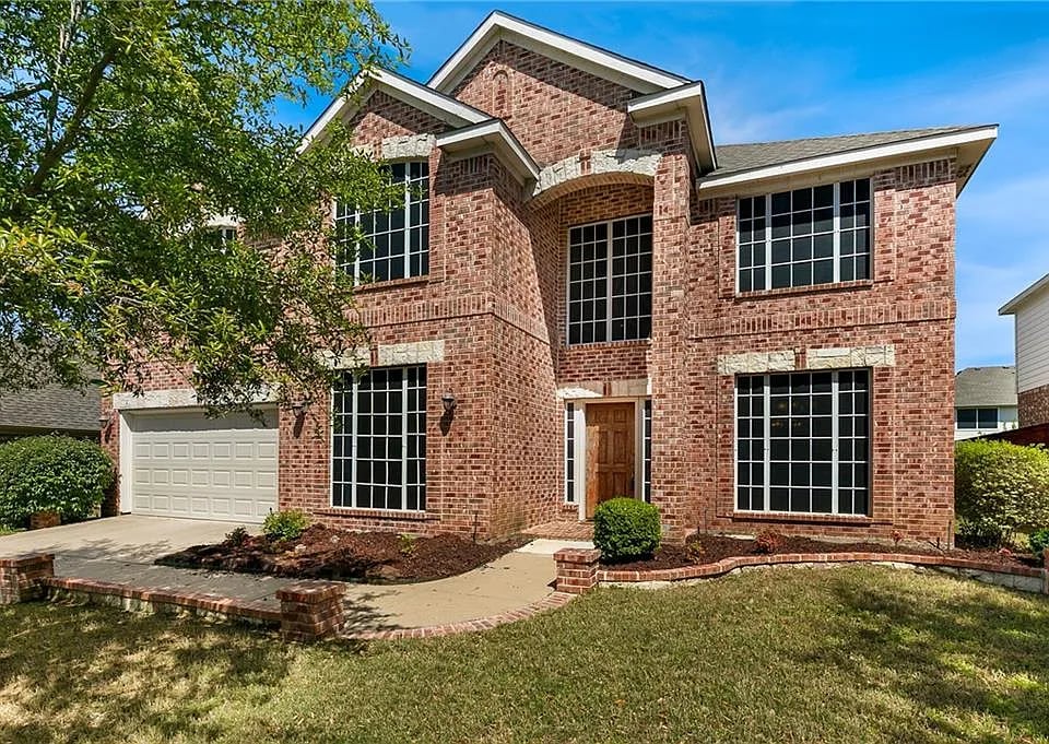 Two-story red brick house with a front-facing garage and tall grid-pane windows.