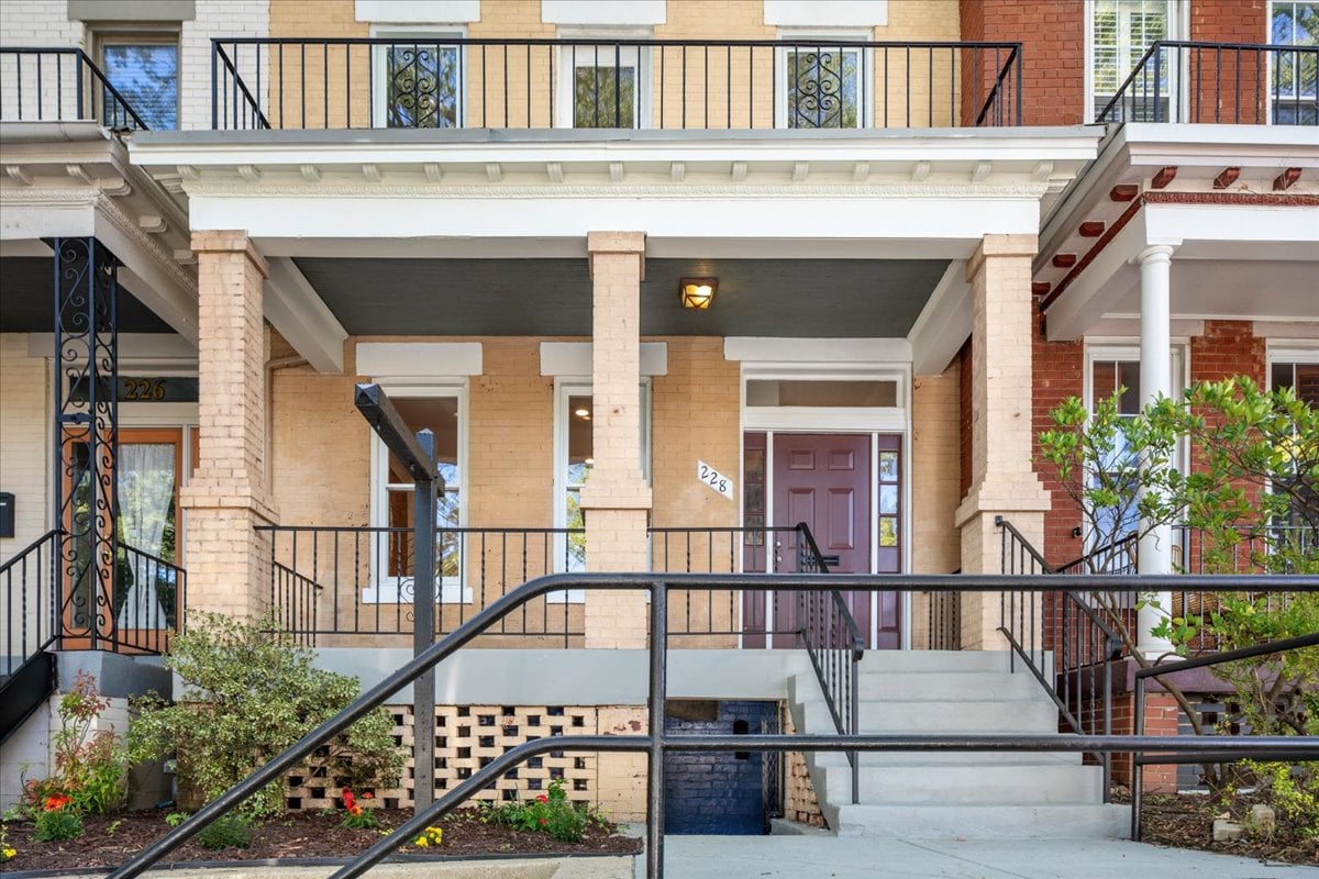 Brick row house with a purple front door, covered porch, and broad steps with black railings.