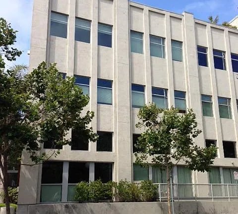 Multi-story apartment building with a light facade, rows of windows, and trees in front.