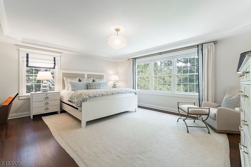 Bright bedroom with a white bed, large tree-view window, and pale seating.