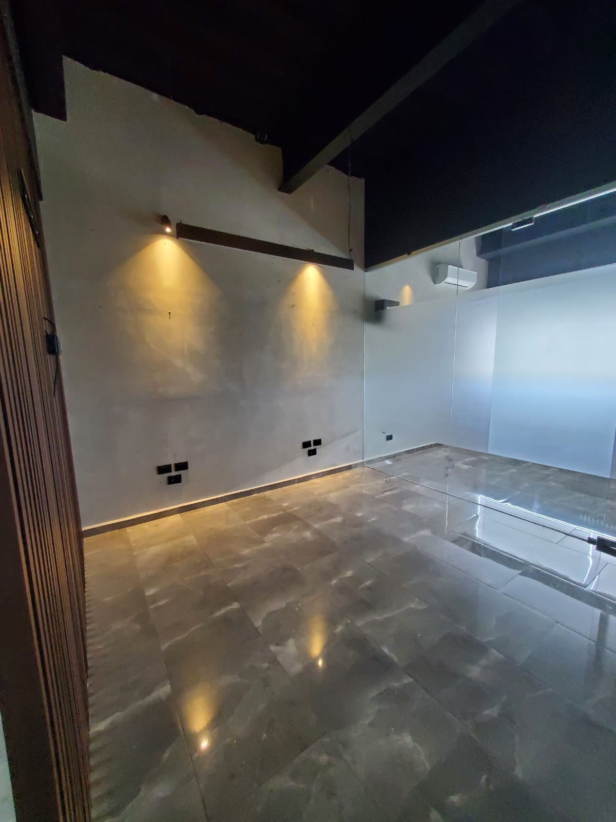 Vacant office with polished tile floors, warm wall lights, and a glass partition.