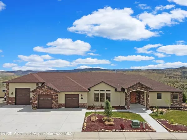 Single-story home with multiple garage bays and stone accents, set against open hills.