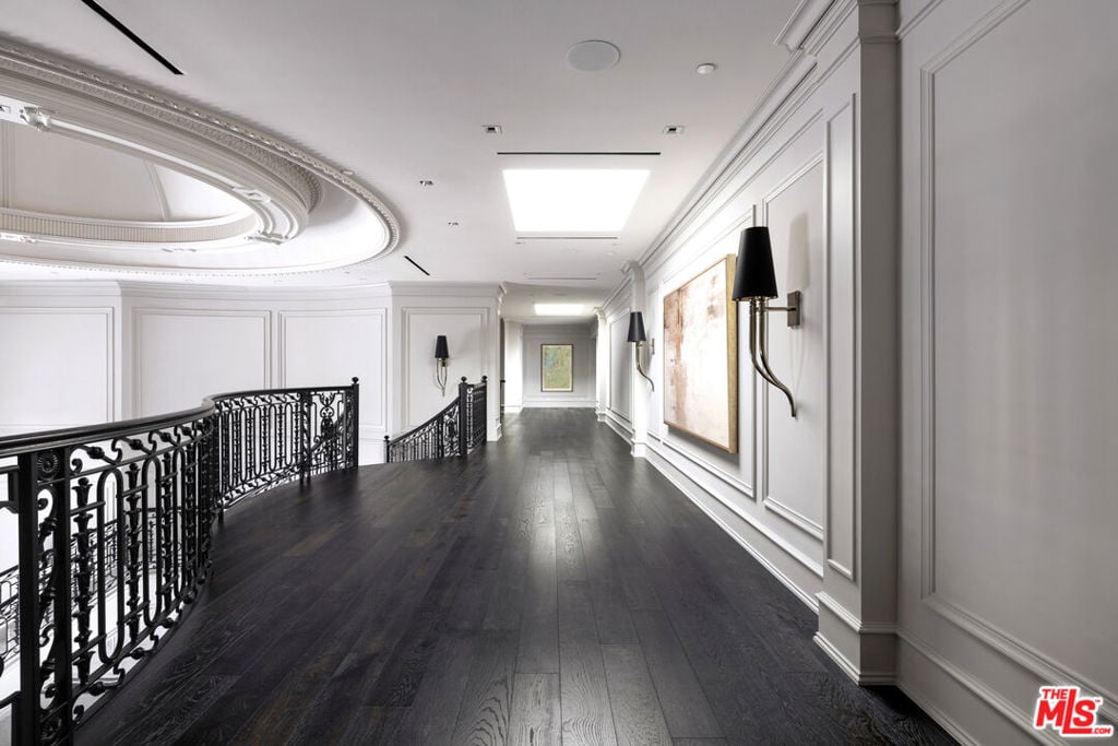Upper-level hallway with dark wood floors, white paneled walls, and ornate black wrought-iron railings.
