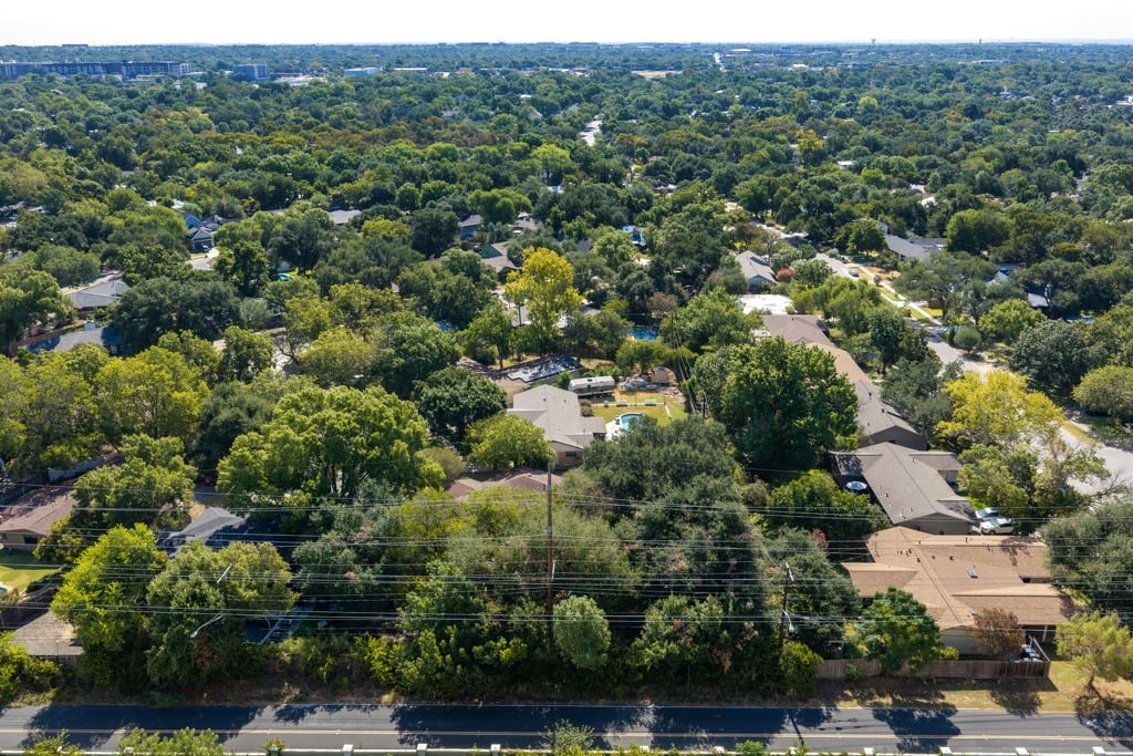 Aerial view of a tree-lined neighborhood, with homes and a road crossed by overhead utility lines.