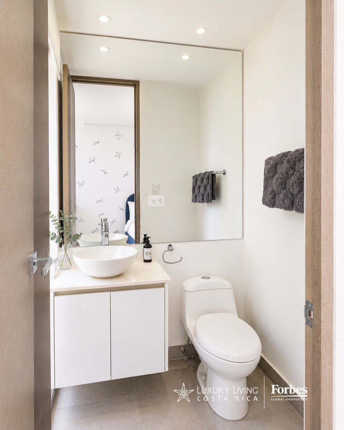 Modern bathroom with a white vessel sink, floating vanity, large mirror, and gray tile floor.