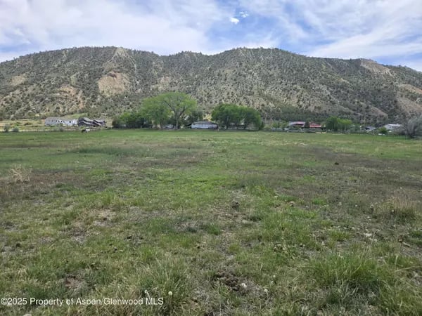 Open grassy land beneath a rugged mountain ridge, with scattered homes along the far edge.