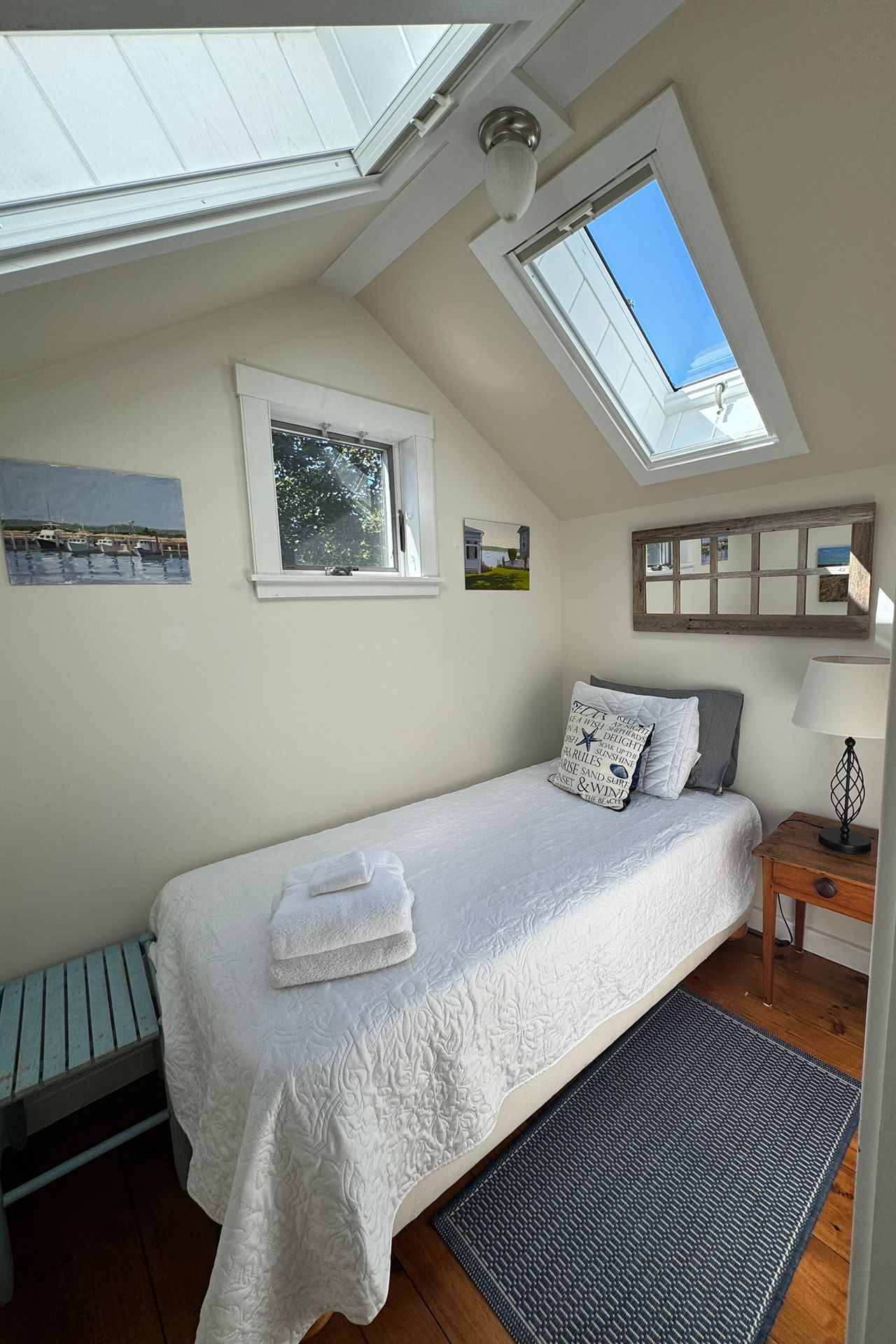 Bedroom with a white quilted bed beneath two skylights and a small window.
