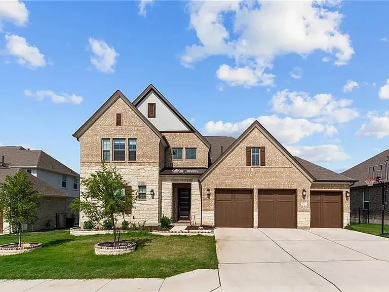 Two-story stone house with steep gables, a three-car garage, and a landscaped front lawn.