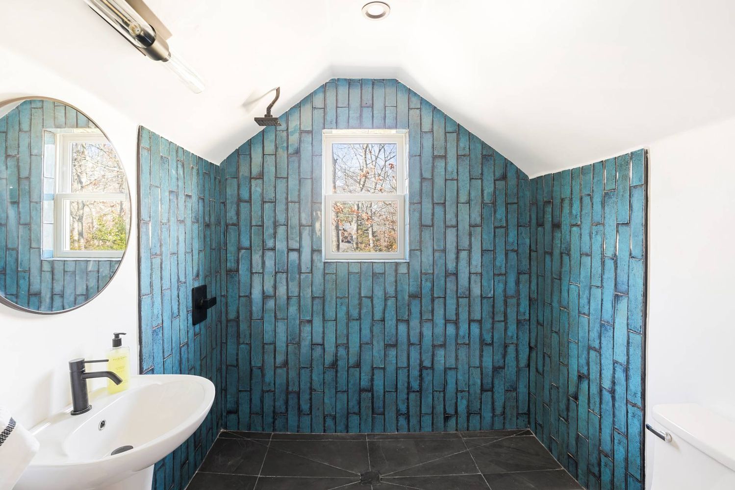 Bathroom with a blue-tiled walk-in shower, central window, and pedestal sink.