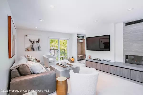 Contemporary living room with a gray sofa, white chairs, sliding glass doors, and a linear fireplace.