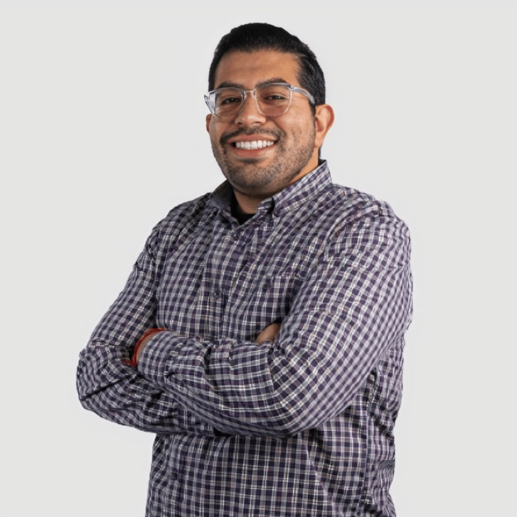 Darrick Ramos smiling with his arms crossed, wearing glasses and a dark plaid shirt.