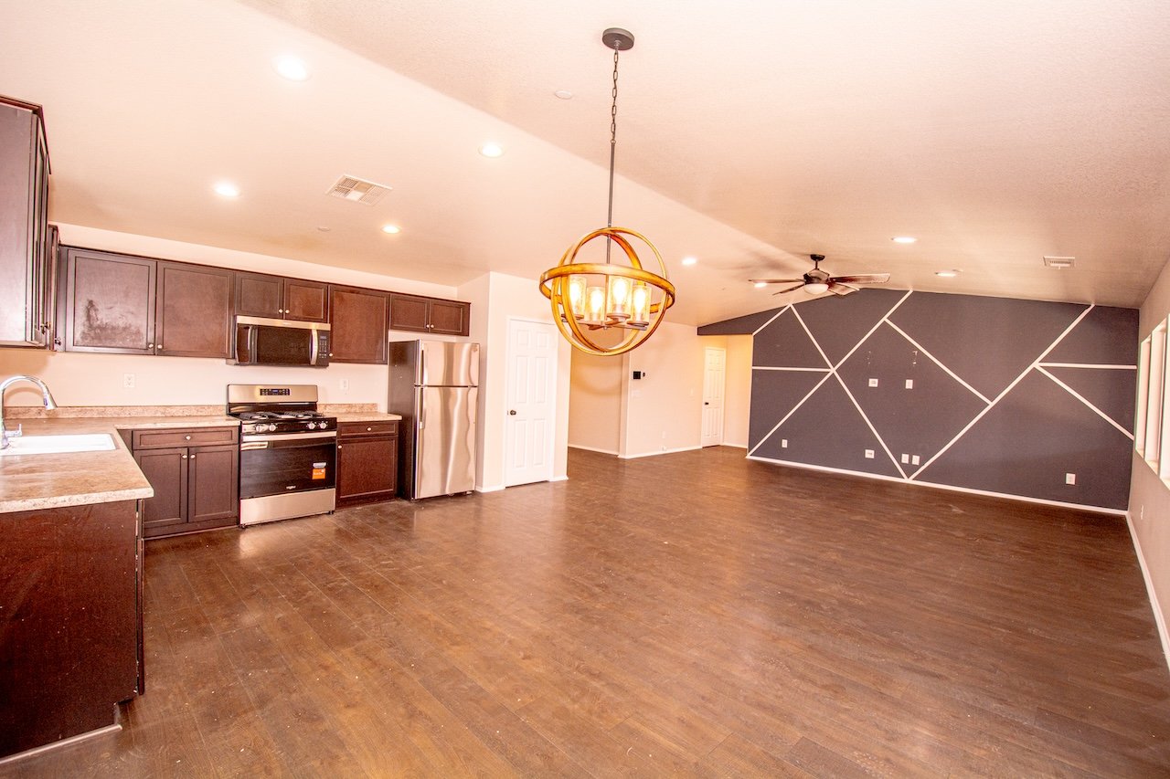 Vacant open-plan kitchen and living area with stainless steel appliances and a geometric accent wall.