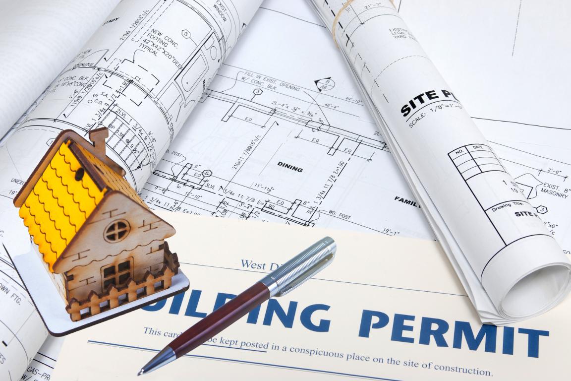 Building permit and architectural plans with a wooden model house and pen.