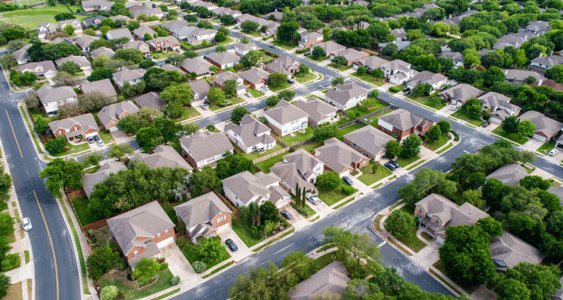 Aerial view of detached homes and leafy yards along winding neighborhood streets.