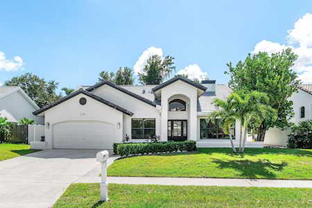Single-story white house with an arched entry, two-car garage, palm trees, and a sunny front lawn.
