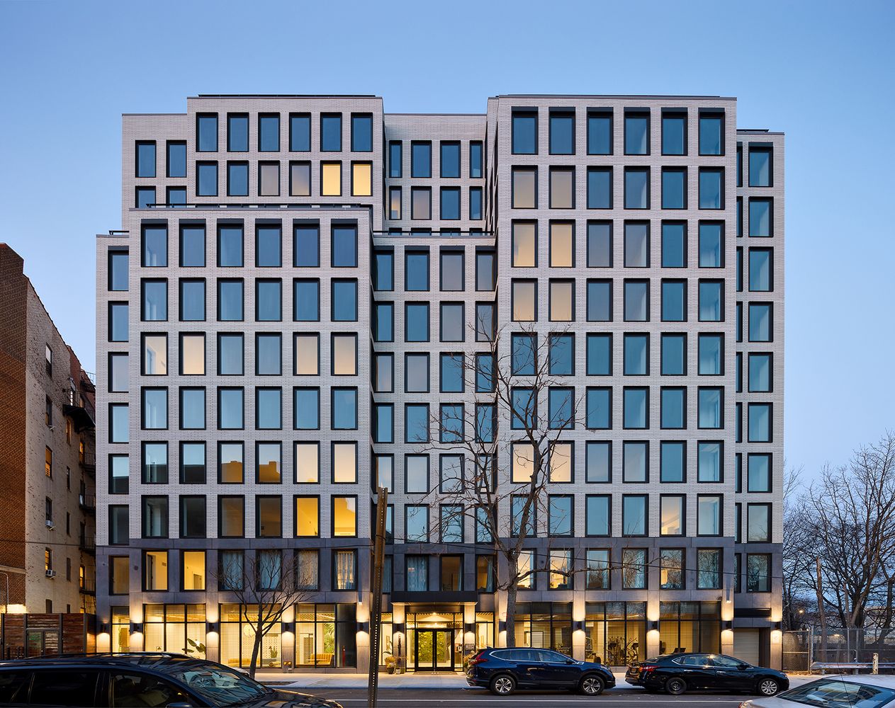 Modern mid-rise apartment building featuring a white brick facade with a uniform grid of large, dark-framed windows.