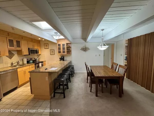 Kitchen and dining area with a large island, wood cabinetry, and exposed ceiling beams.
