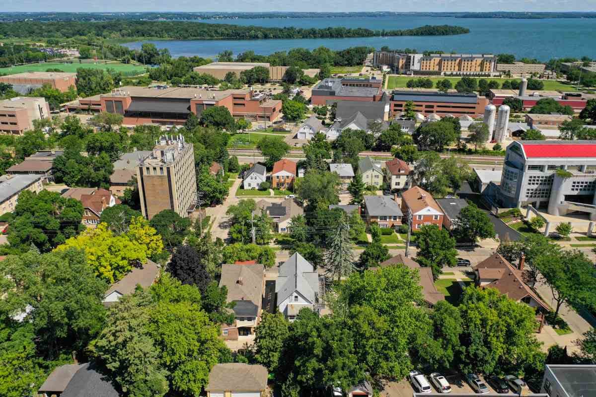 Aerial view of a Madison, Wisconsin neighborhood in summer, with single-family homes, apartment buildings, and larger institutional buildings along a lakeshore.