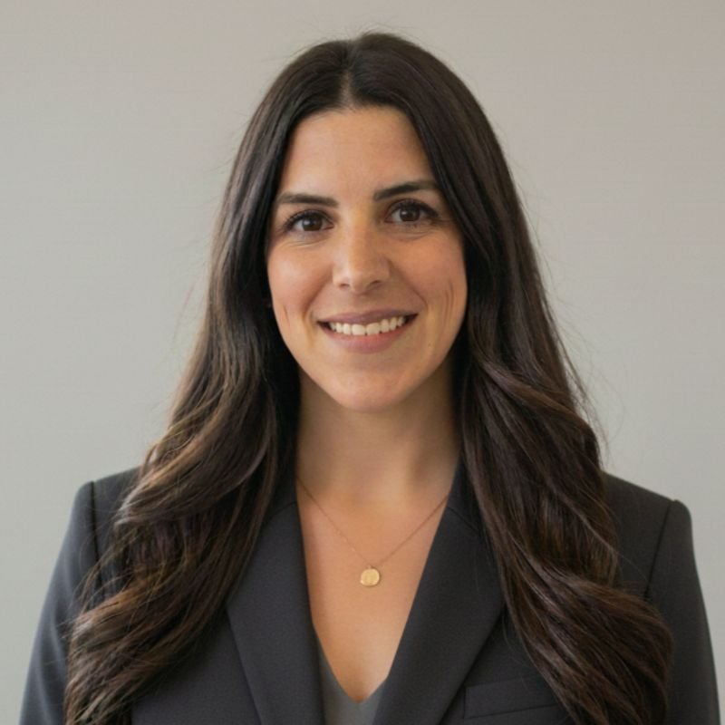 Brittney King in a dark blazer and gold pendant against a light wall.