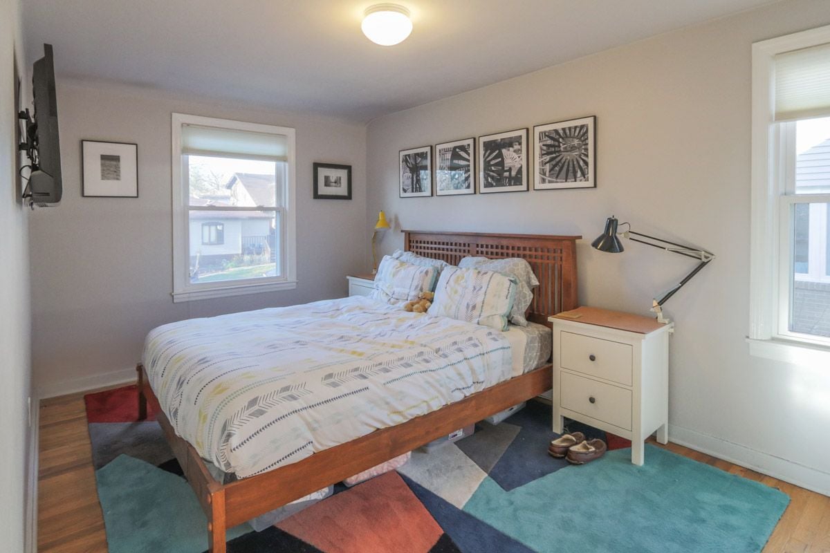 Furnished bedroom with a wooden platform bed, framed prints, and colorful geometric rugs.