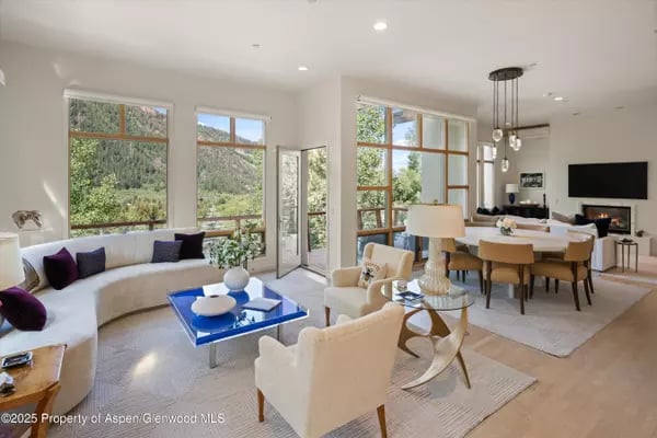 Open-plan living and dining room with large windows overlooking wooded mountain slopes.