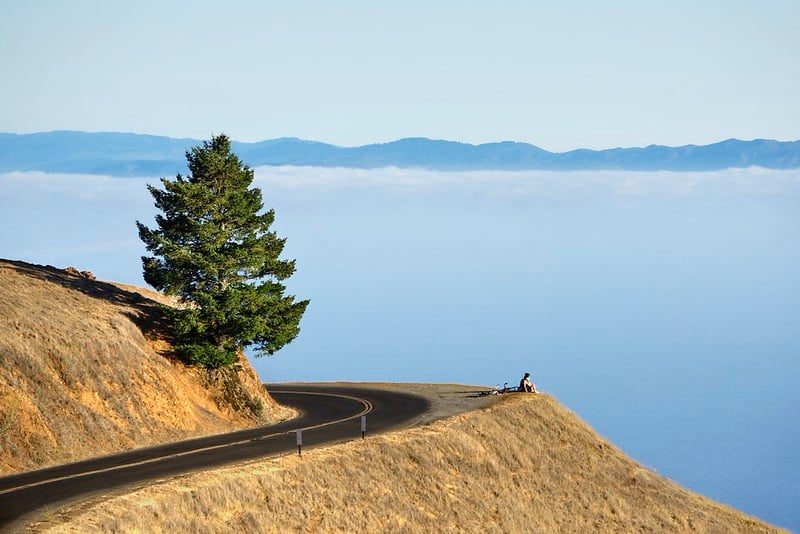 A cyclist rests at Trojan Point on Mount Tamalpais, overlooking a sea of clouds above the Bay Area coastline