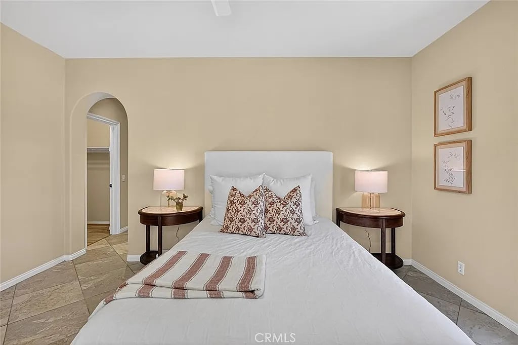 Furnished bedroom with a white bed, patterned pillows, matching bedside tables, and an arched doorway.