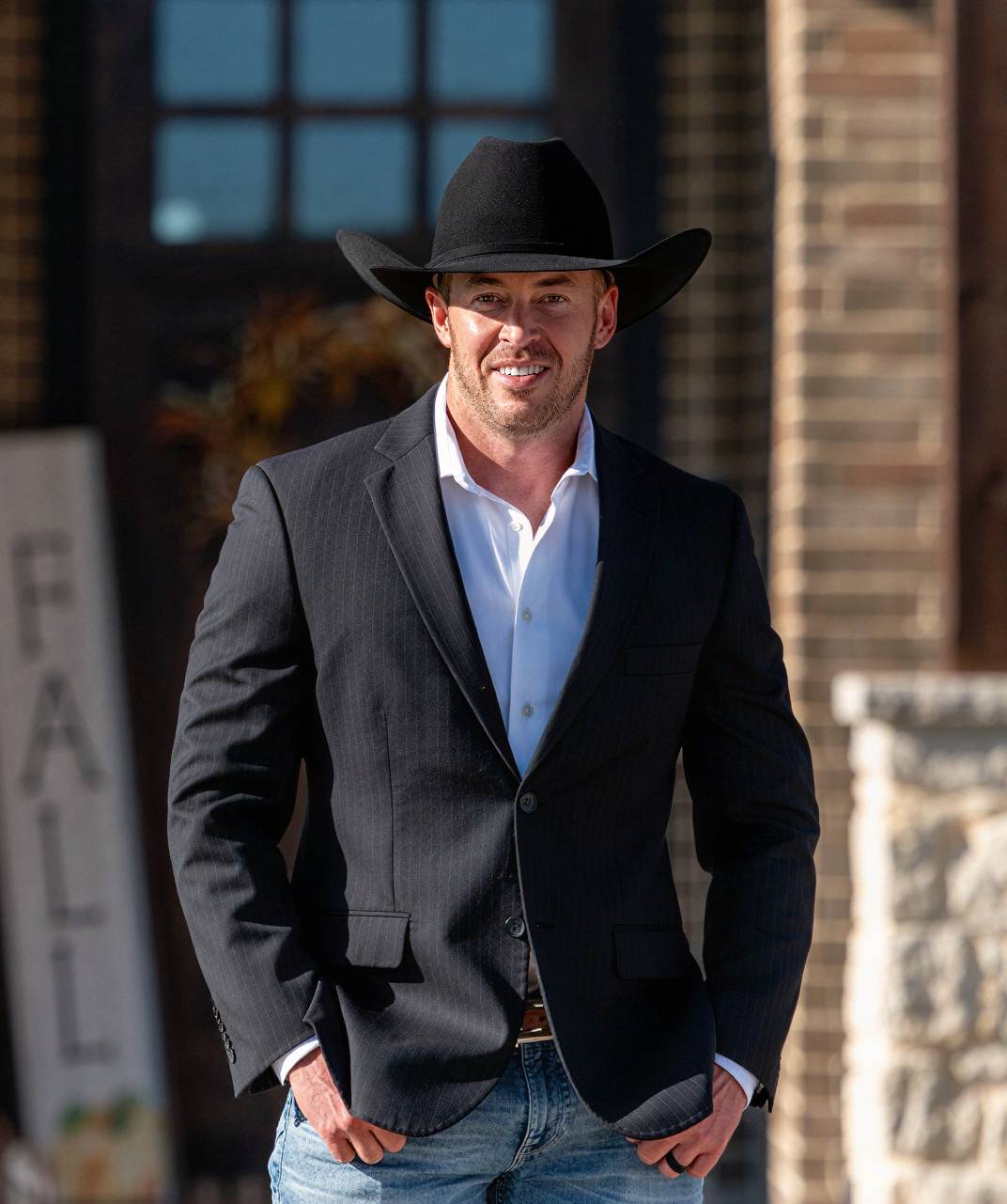 Daniel Sparkman wearing a black cowboy hat and suit jacket outside a brick building.
