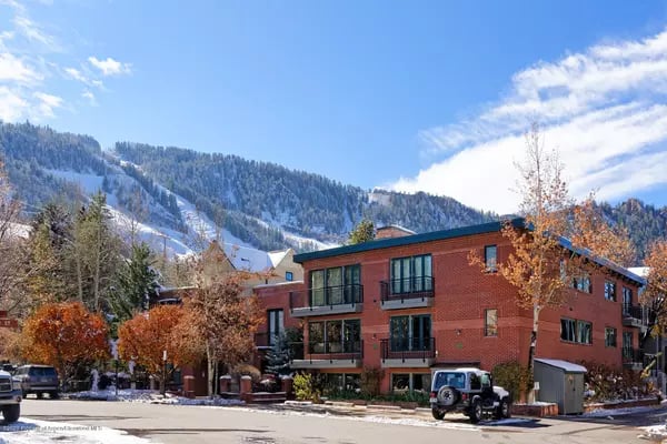 Red-brick multi-story building with balconies beneath snow-dusted mountains.