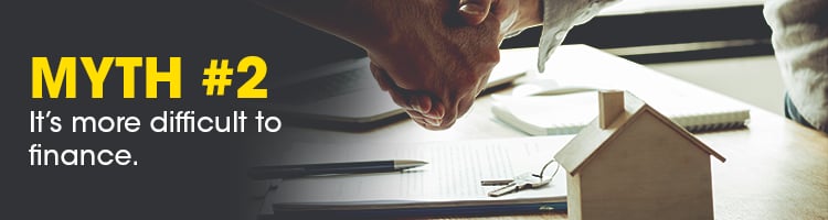 Myth #2: It’s more difficult to finance. A hand reaches for keys beside paperwork and a model house.