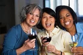 Three smiling women raise glasses of wine together indoors.