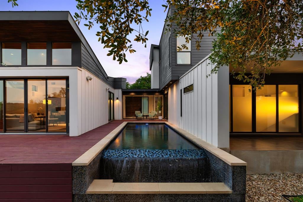 Modern home with a courtyard reflecting pool, waterfall, and reddish wood deck at dusk.