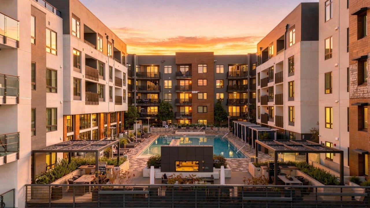 Apartment courtyard with a central swimming pool, balconies, and outdoor seating at sunset.