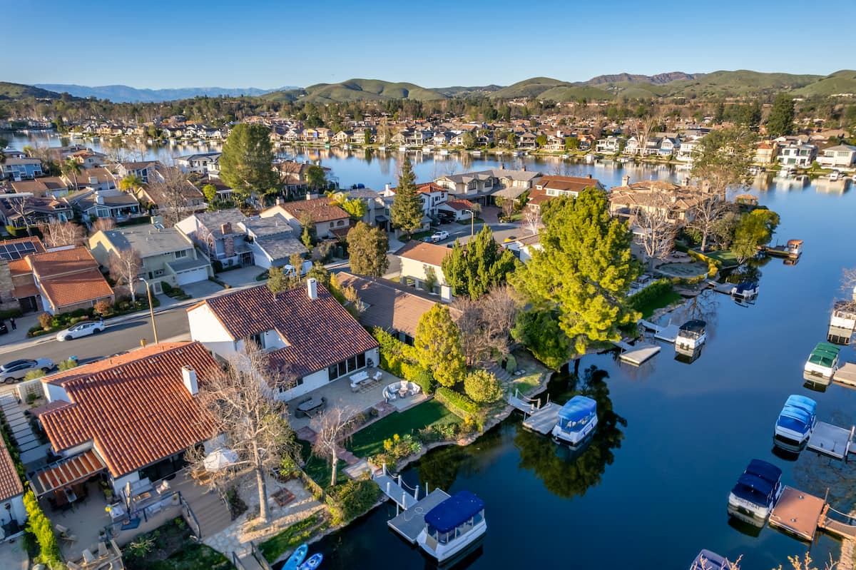 Aerial view of lakeside homes with private docks, boats, and rolling hills beyond.