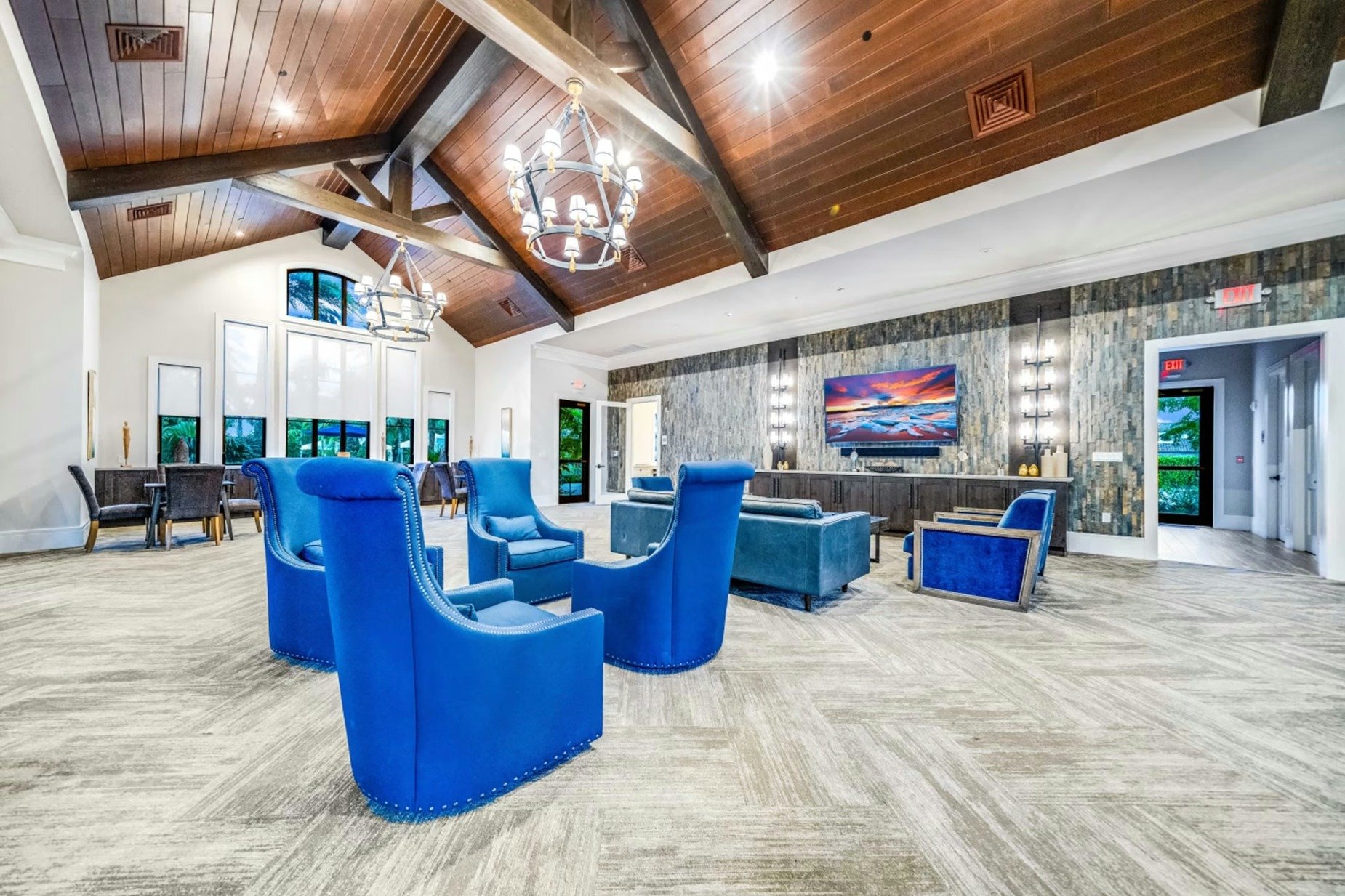 Communal lounge with blue armchairs, a stone accent wall, and a vaulted wood ceiling.