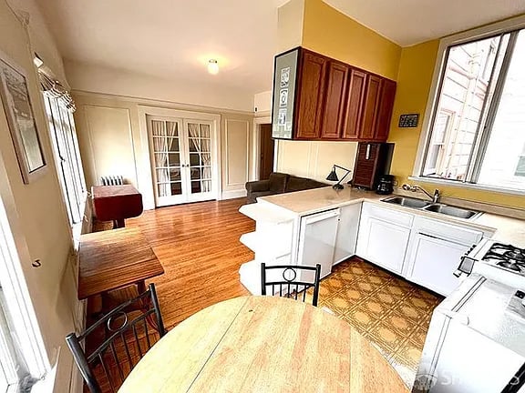 Apartment kitchen and dining area with white cabinets, a large window, and hardwood floors.