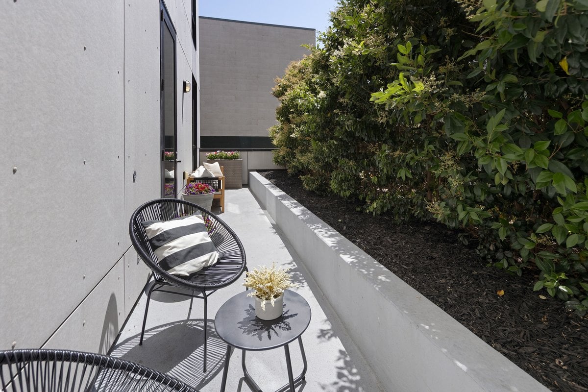 Private patio with black wire seating, a small table, and a raised planter of shrubs.
