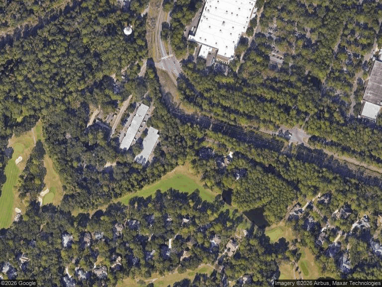 Aerial view of wooded homes and roads beside a green golf course fairway.