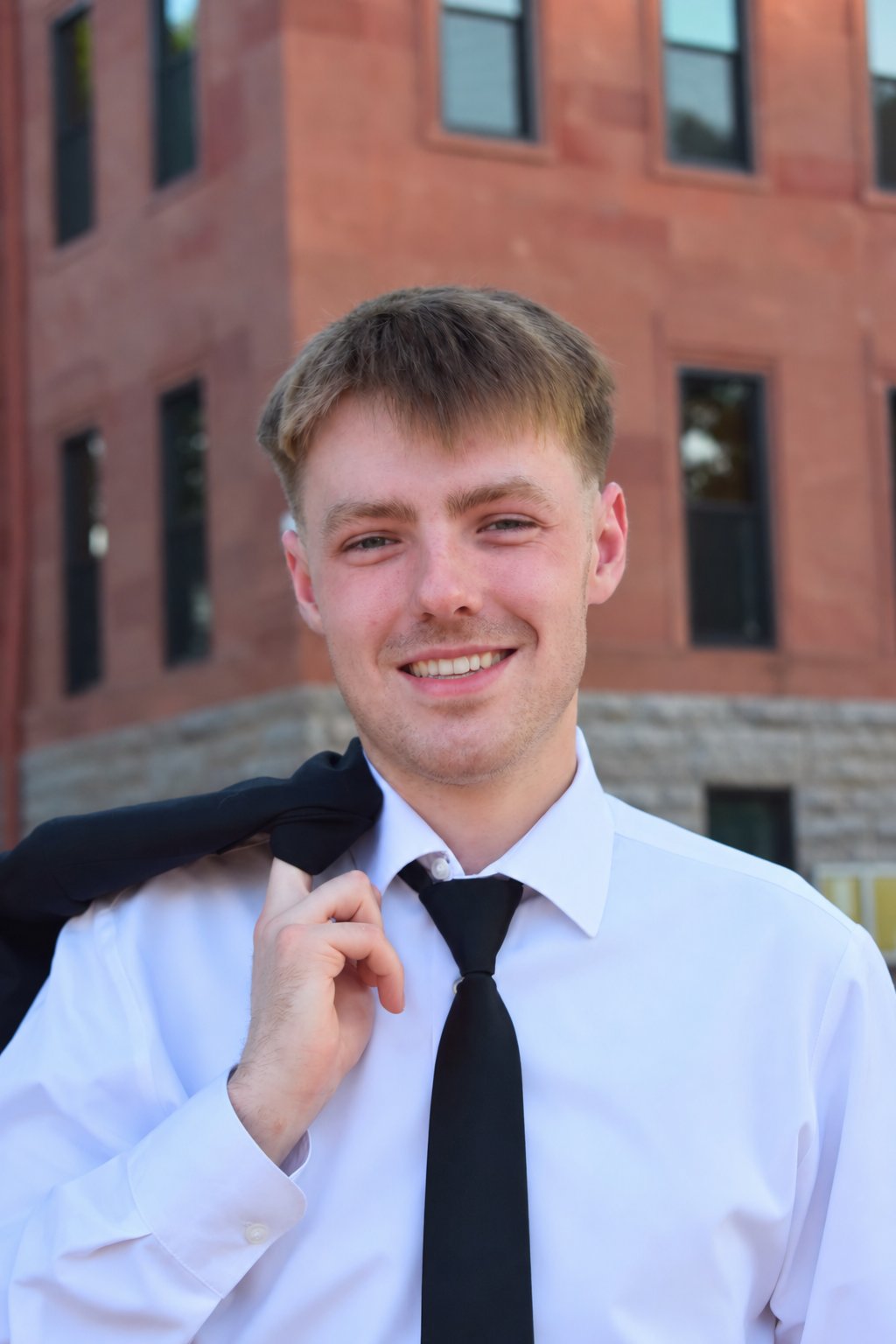 Luke Williams in a white shirt and black tie, holding a jacket over his shoulder.