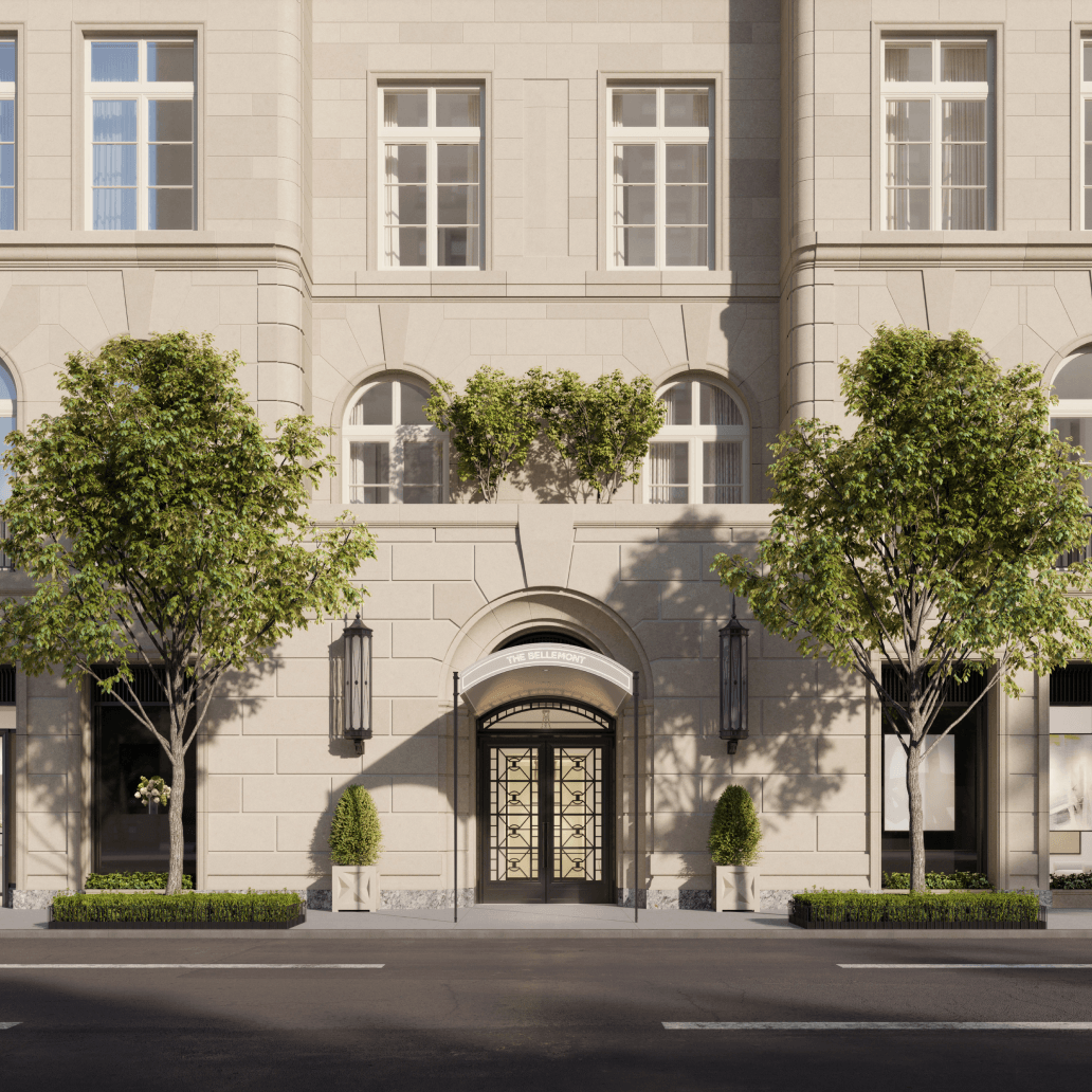 Pale stone residential building with a grand arched entrance and leafy trees along the sidewalk.