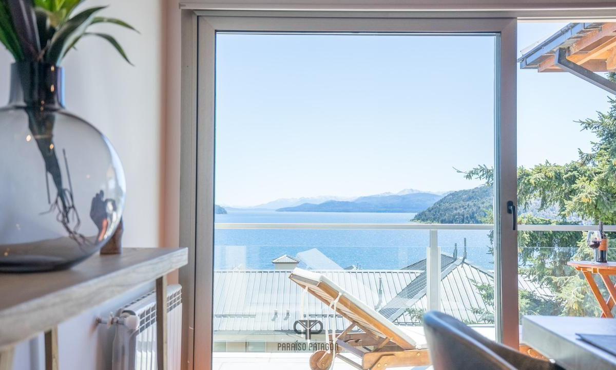 Apartment interior opens onto a balcony with a lake and mountain view.