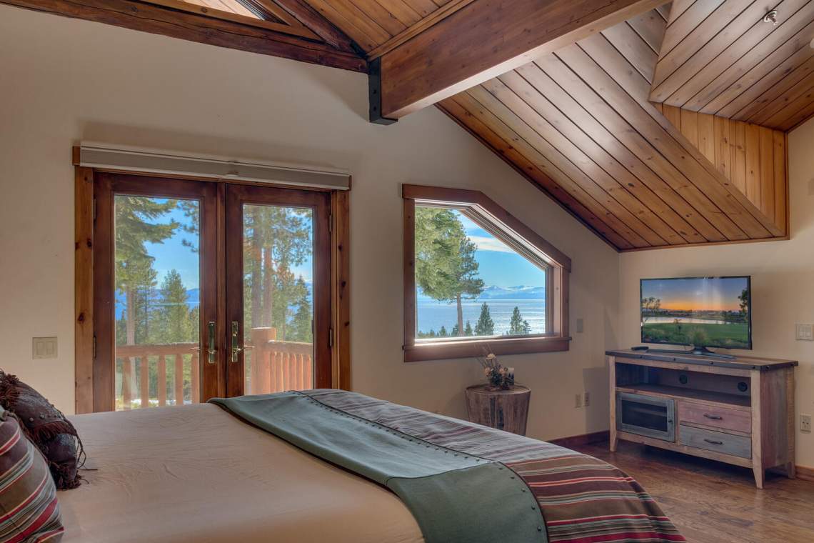 Bedroom with a vaulted wood ceiling and lake and mountain views through the windows.