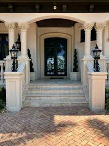 Home entrance with white columns, stone steps, lanterns, and a herringbone brick driveway.